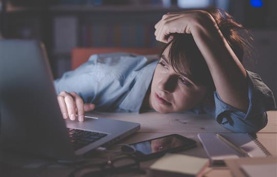 young woman with head resting on her desk while on her computer with a bored look on her face