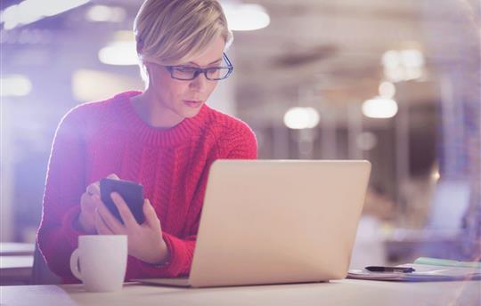 An email marketer looking intently between her cellphone and her laptop