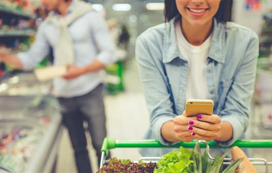 Woman pushing a shopping car in the supermarket, looking at her phone