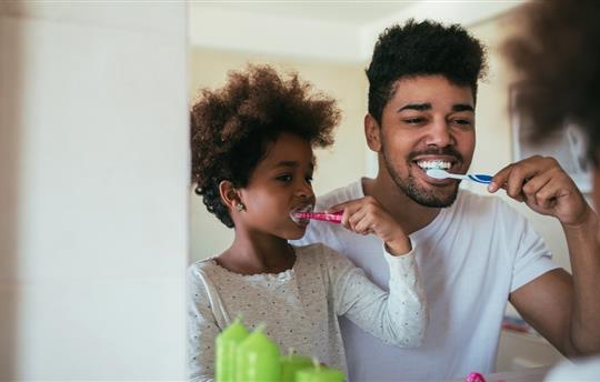 Father and daughter brushing their teeth in front of bathroom mirror