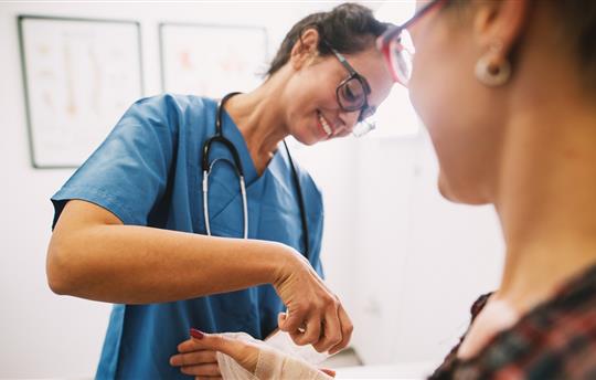 Professional nurse at the hospital bandaging the hand with a medical bandage for a woman patient.