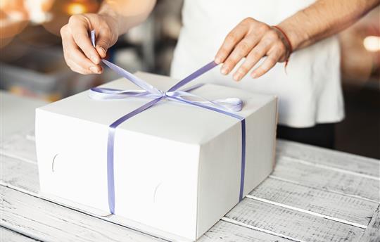 Young cook ties violet ribbon on white cake packaging