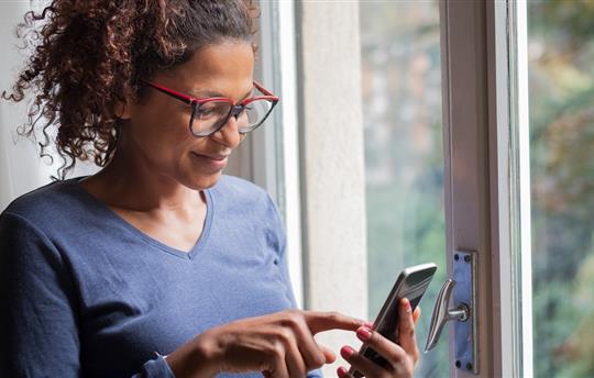 woman smiling near window reading phone message