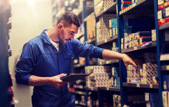 auto mechanic looks at auto parts organized on a shelf