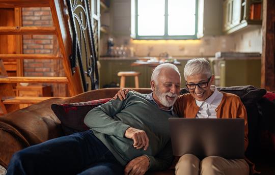 an older gentleman and woman laugh while looking at a laptop screen