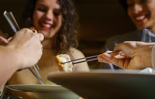 group of smiling young friends eating dim sum dumplings at a restaurant