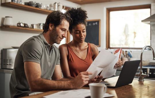 Cropped shot of a couple using their laptop and going through paperwork at home