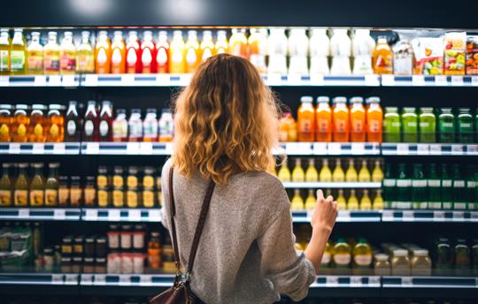 back view of young woman looking at bottle of juice in grocery store