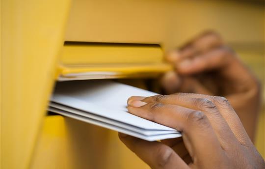 hand reaches into row of mailboxes for mail