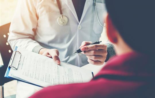 doctor pen and handing clipboard with forms over to patient in office setting