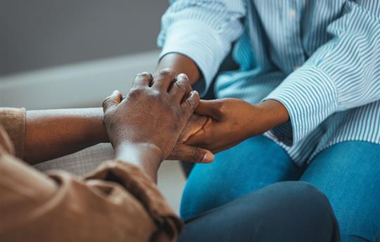 Close-up shot of two unrecognizable people holding hands in comfort at home.