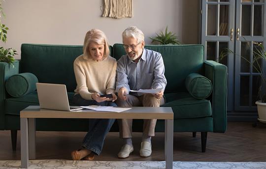 Smiling elderly spouses paying bills online using laptop