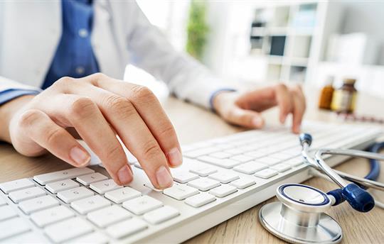 The hands of a female doctor typing on a keyboard