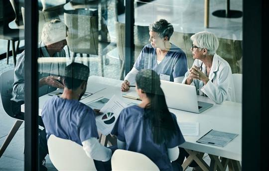 Healthcare team sitting at a table in blue scrubs having a meeting
