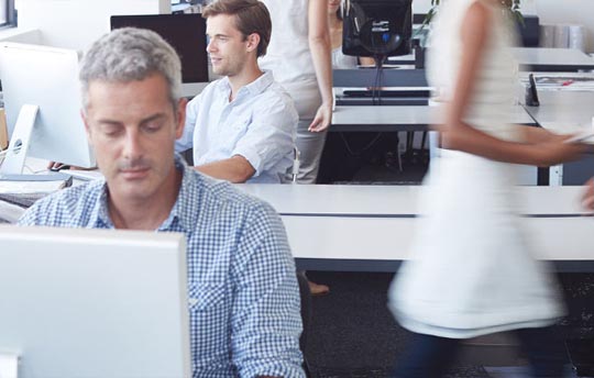 man looking at a large monitor with office workers at work behind him