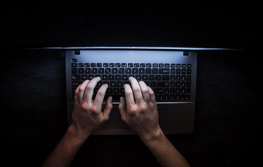 The hands of a hacker type on a keyboard in the dark
