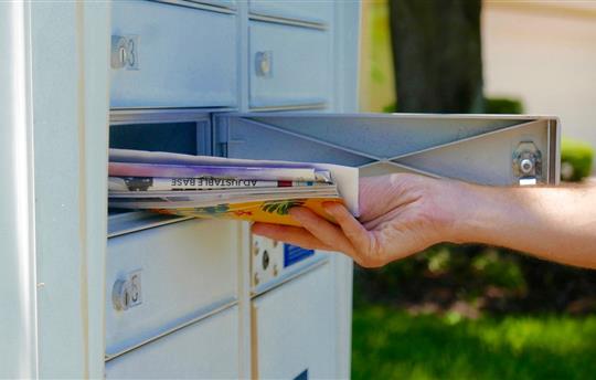 A hand is pulling a pile of mail out of a mailbox
