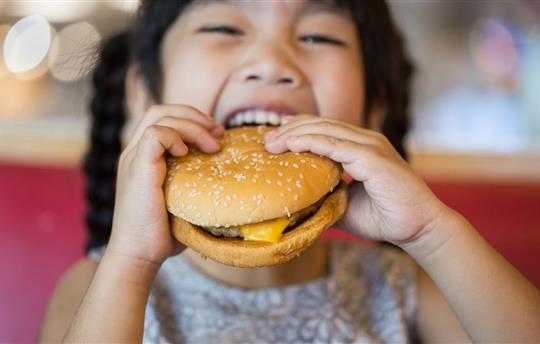 child eating cheeseburger in food court