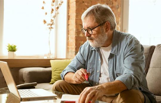 Senior man sitting on his sofa and working with laptop at home.