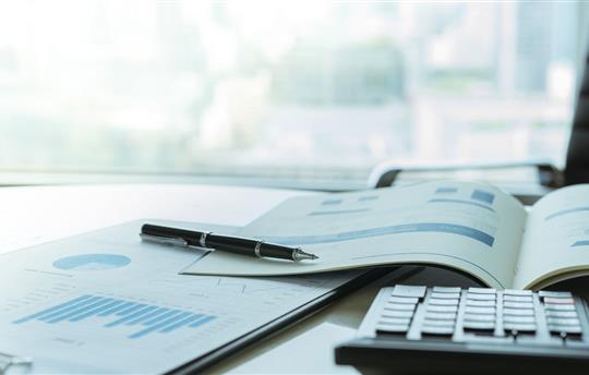 Pen with business report and calculator on financial advisor desk.