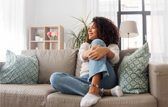 woman sitting on couch in a room full of natural light and appearing happy