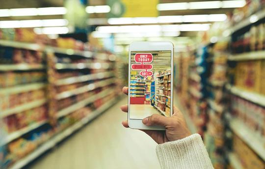 hand holding up a smartphone with a picture of the grocery aisle on it