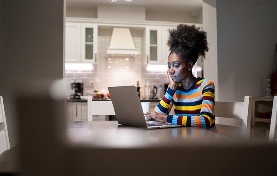 woman sitting at her dining room table at home looking at her laptop