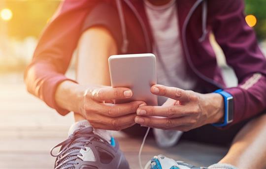 Person dressed for exercise, sitting on the ground checking fitness app on smartphone