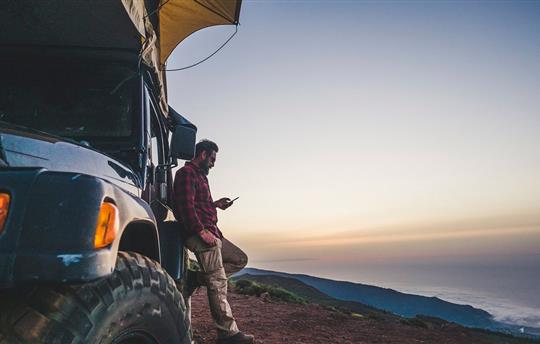 man leaning against his SUV and looking at phone as the sunsets near the ocean's edge