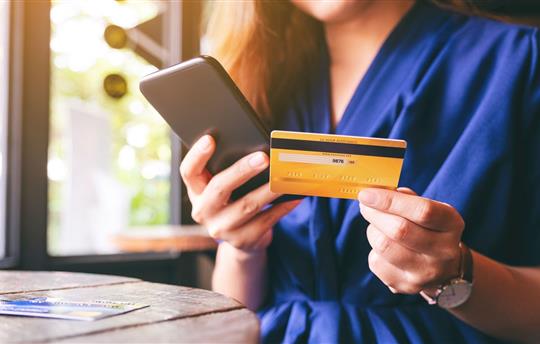 Closeup image of woman in blue dress using credit card for purchasing and shopping online on mobile phone
