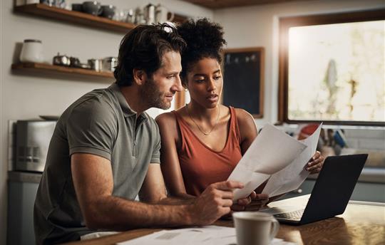 man and woman sitting together looking at paper work and a laptop