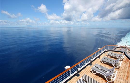 view of the ocean and a cruise ship sundeck filled with striped lounge chairs