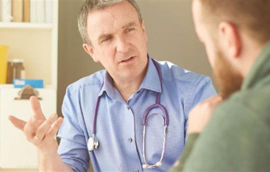 healthcare professional with stethoscope around his neck talking to patient in office
