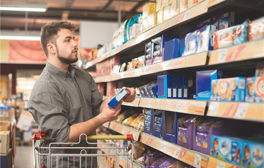 Man stands in a supermarket with a bundle of biscuits in his hands and looks at the shelf with sweets.