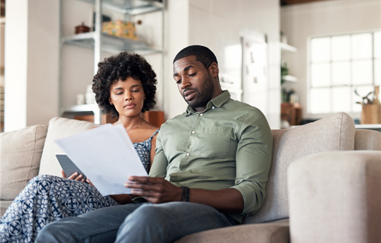 couple sitting together on couch looking at paperwork