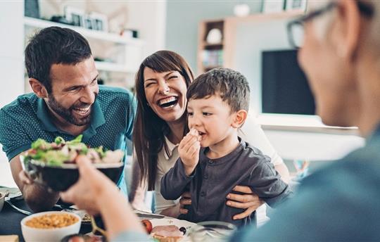 Dad, mom and son having a meal and smiling as they are passing the food to grandma