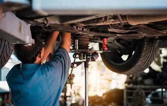 Mechanic repairing a car, mechanic inspects car suspension system and chassis with a torch-lite under the car.
