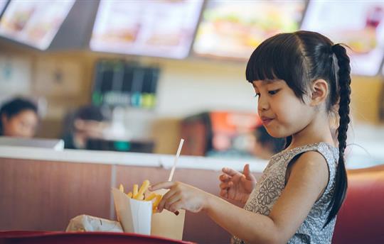 Young girl eating french fries at fast food restaurant