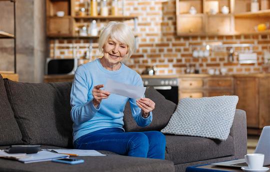 Woman with white hair seated on a couch reading mail