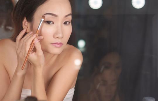 woman looking into a vanity mirror putting on eye shadow