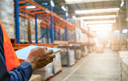 person in orange safety vest holding tablet and checking the stock products in a warehouse