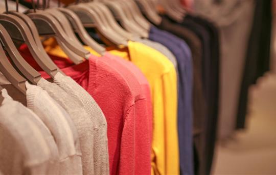 white, pink, and yellow sweaters hanging on a clothing rack