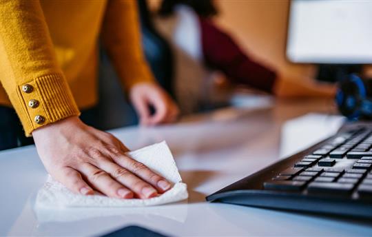 Woman in yellow sweater using a disinfectant wipe to clean desk area