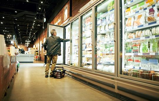 man at grocery store holding door open in the frozen aisle and reaching in