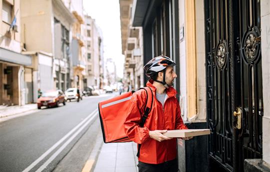pizza delivery man in red jacket and bike helmet delivering one pizza