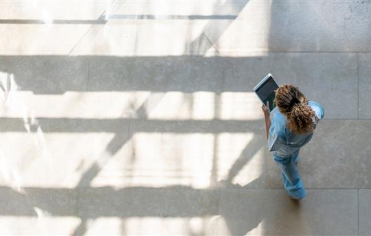 bird's eye view of a female hospital worker in blue scrubs walking and looking at a tablet