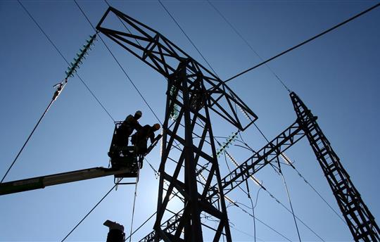 two utility workers on a lift working on power lines with blue sky behind them