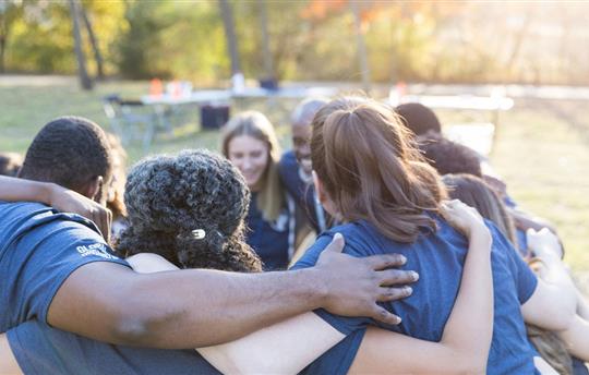 group of volunteers outside standing in a circle with arms on each others' shoulders