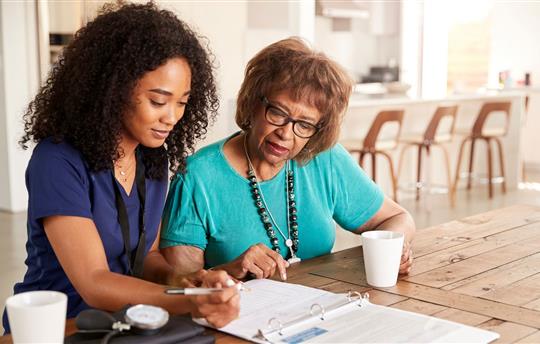 Female healthcare worker filling in a form with a senior woman during a home health visit