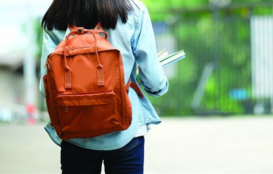 Back of student girl holding books and carry school bag while walking in school campus background